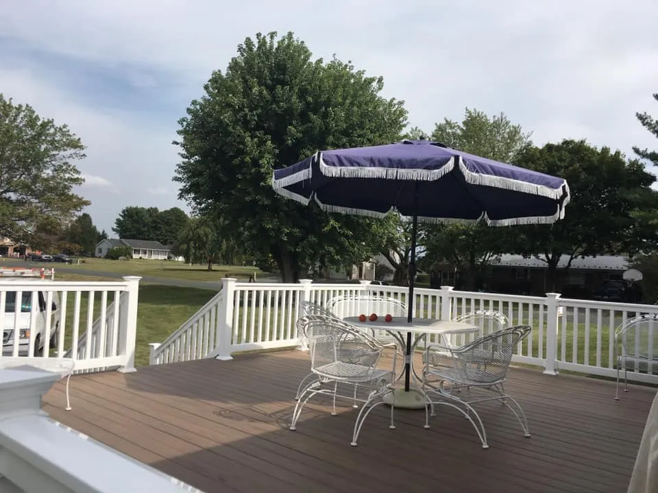 A brown composite deck with white railings, a patio table and a navy umbrella