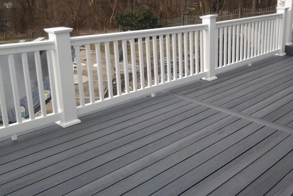 A gray composite deck with white square-baluster railings, beside a backyard pool