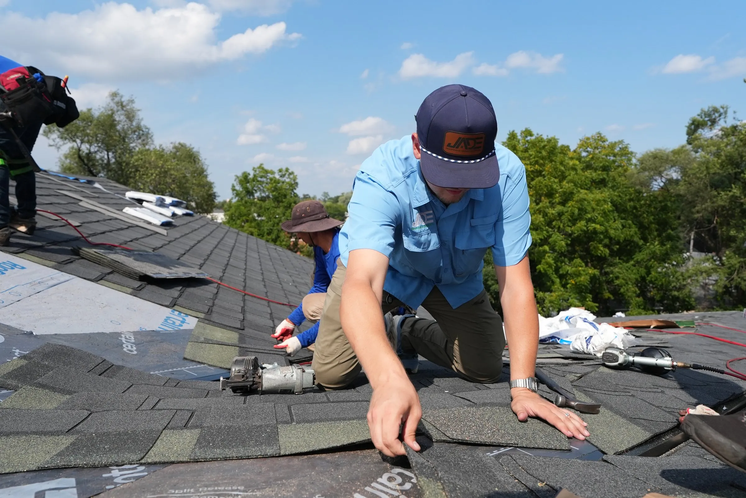A Jade Roofing & Construction crew member fastening new architectural shingles on a residential roof