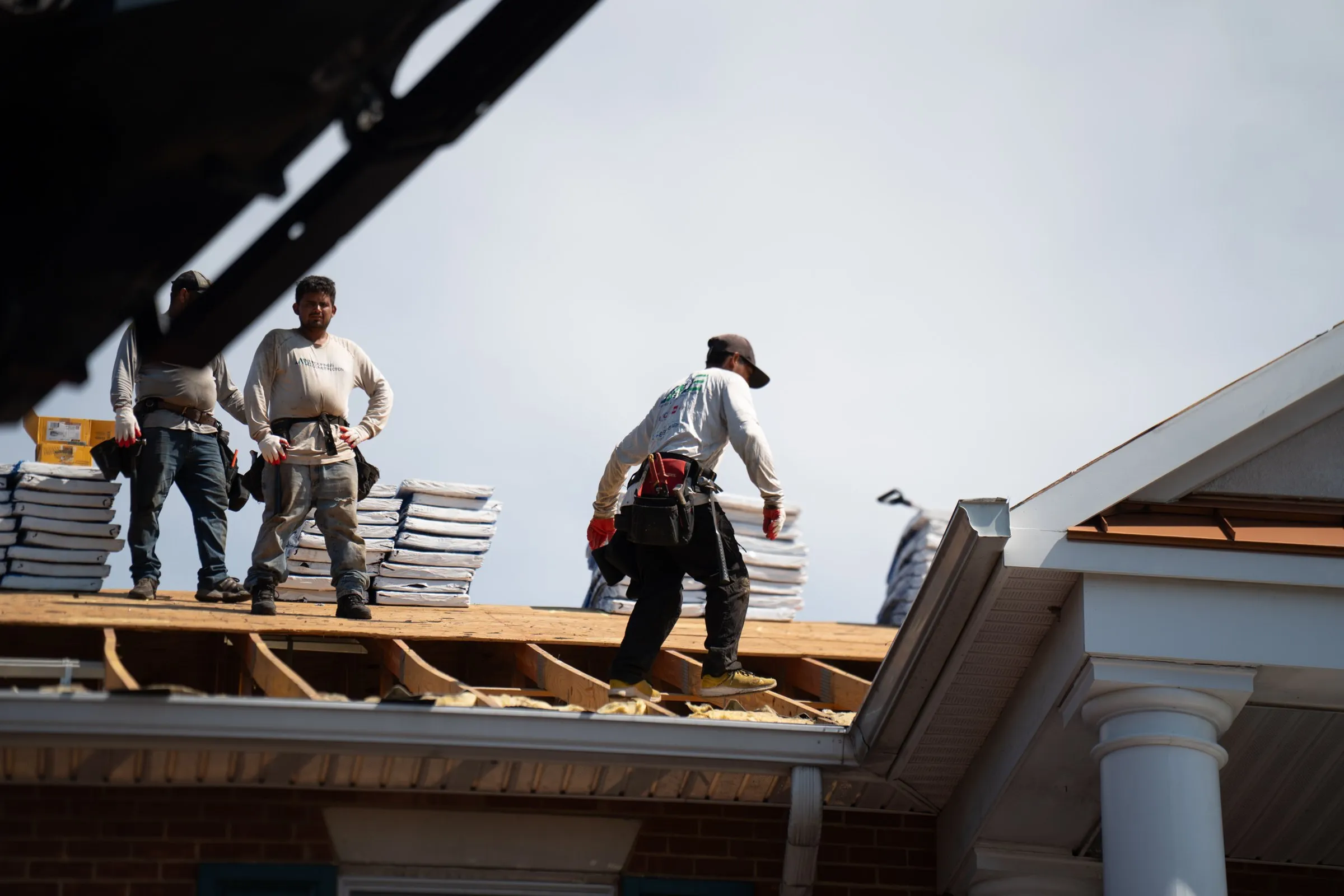 Jade Roofing & Construction crew members on a roof deck during a tear-off, with bundles of new shingles staged