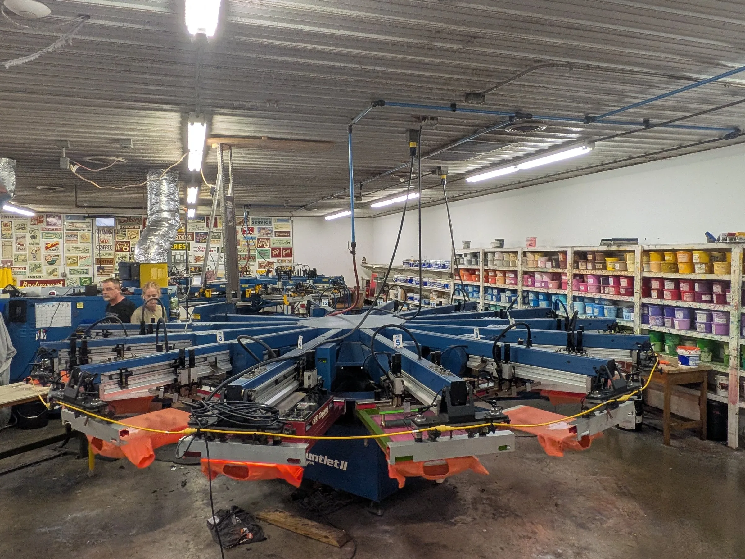 Del Print's automatic screen printing presses running orange shirts on the production floor in Greencastle, Pennsylvania, with walls of ink behind